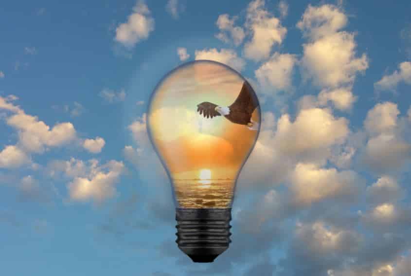 getting a patent starts with an idea, picture is a light bulb against the blue sky, containing an eagle in flight in front of a sunset background