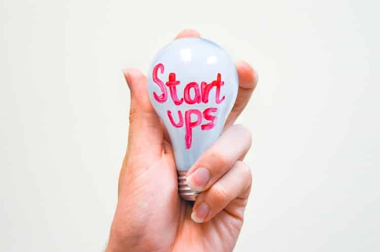 Hand holding a light bulb with "startups" written on it