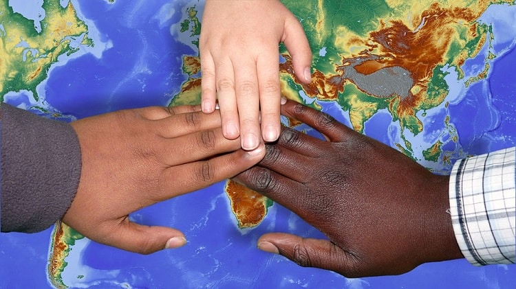 People of different color touching their hands above a world map