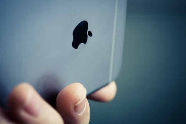 Apple Logo design on iPhone shown in hand with fingers on blue background